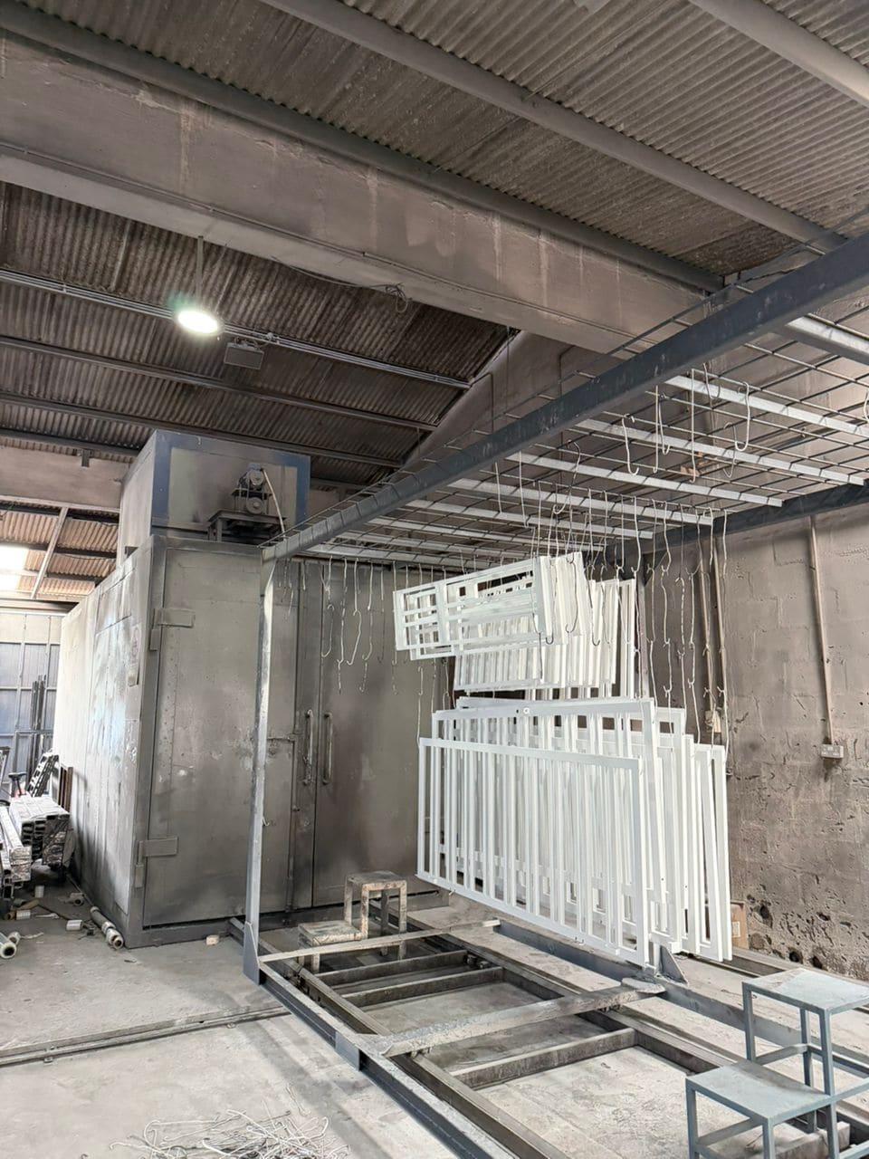 Rows of freshly powder-coated white grilles hanging to cure beside the curing oven