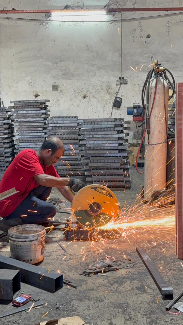 Worker cutting a steel bar on an abrasive chop saw, sparks flying, in the Tenn workshop