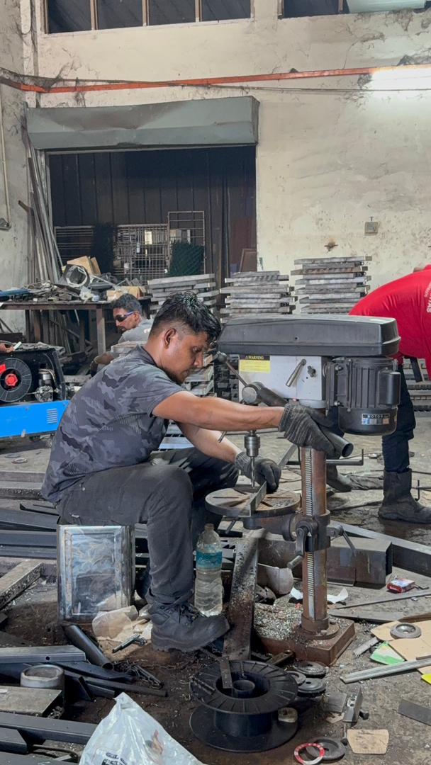 Two fabricators grinding and welding steel grille frames on the workshop floor
